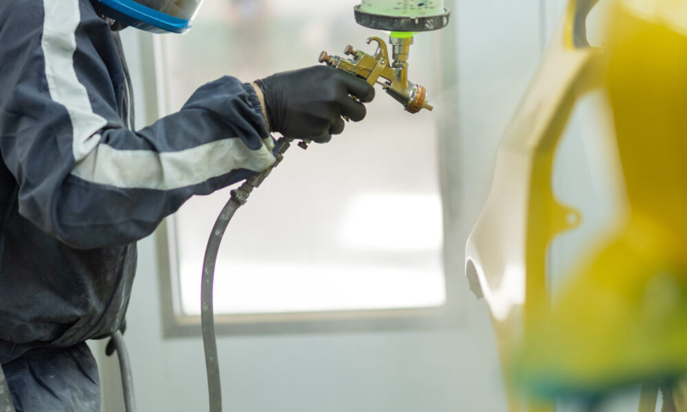 image of Straight-N-Paint employee spray painting a customer's car yellow in Rangiora auto workshop