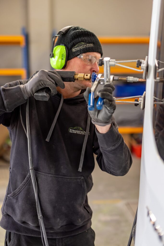 Straight-N-Paint auto repairer performing panel beating on a car in the Rangiora workshop