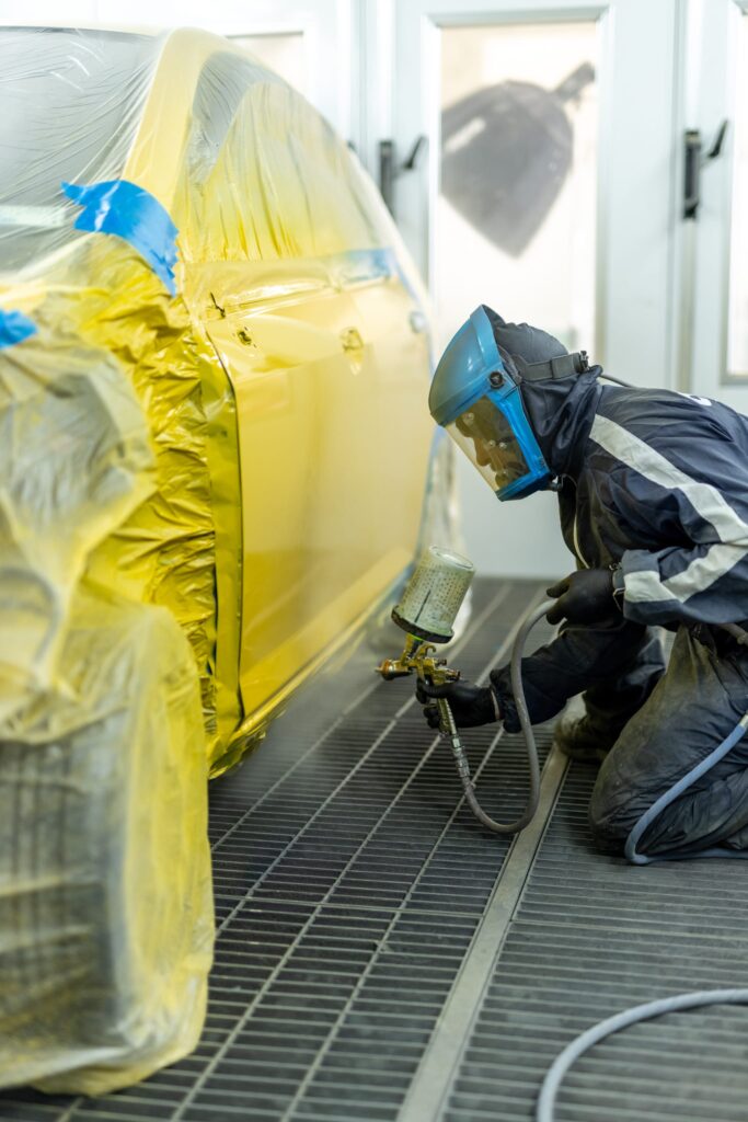 image of Straight-N-Paint employee spray painting a customer's car yellow in Rangiora auto workshop