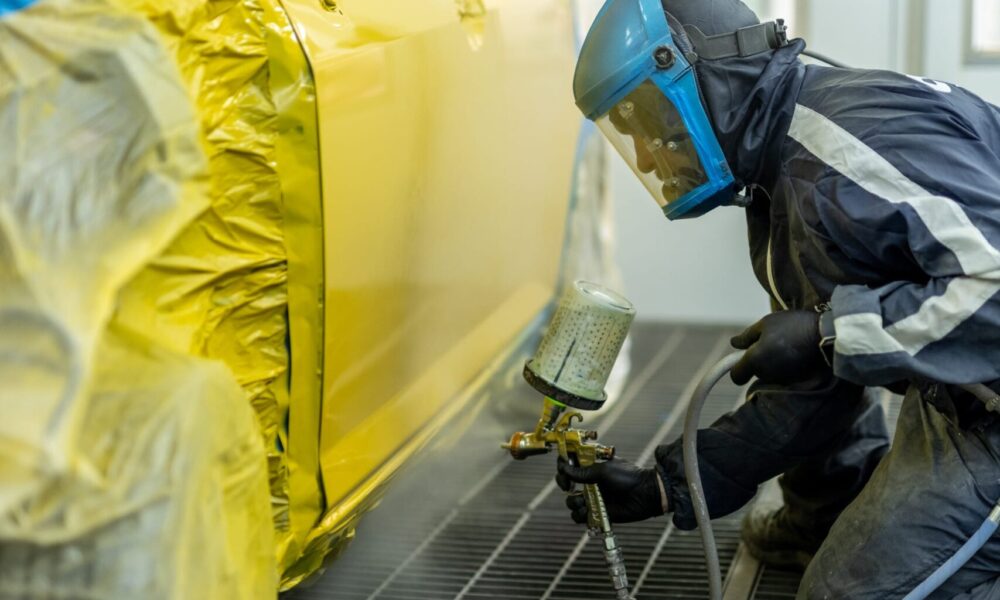 image of Straight-N-Paint employee spray painting a customer's car yellow in Rangiora auto workshop